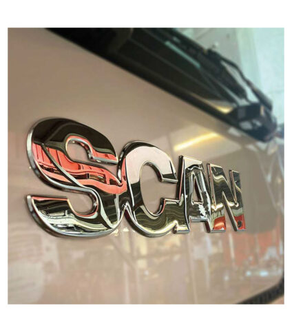 Logotipo cromado de veículo, fundo desfocado.